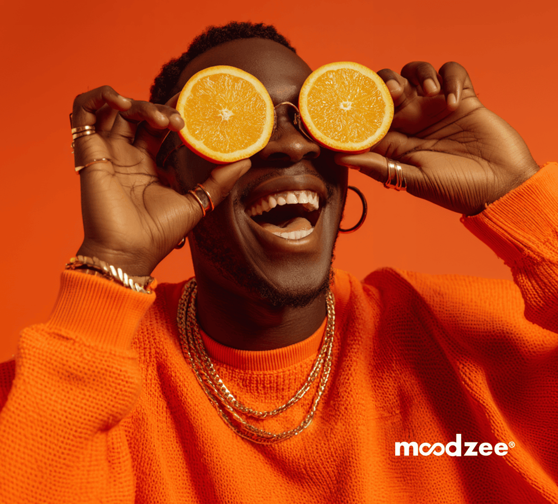 Man in orange sweater smiling and holding orange slices over his eyes against orange background - Moodzee orange essential oil