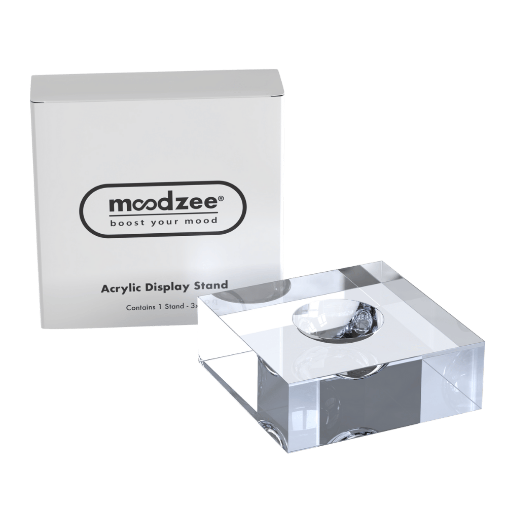 A clear acrylic display stand with a circular recess in the center, shown in front of its white branded box labeled 'moodzee'. 