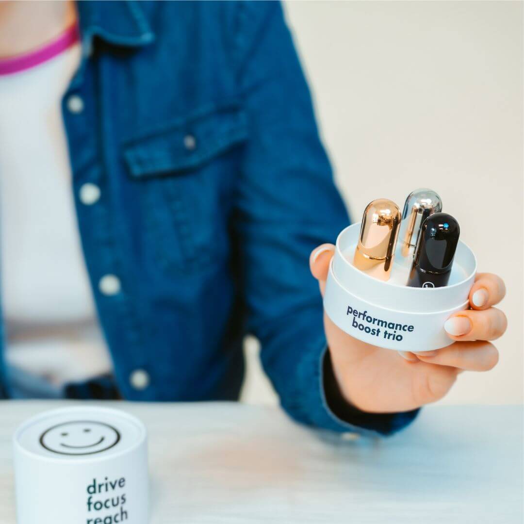 Woman holding Drive, Focus, and Reach roller balls with the open Performance Boost box, black, silver, and gold pill bottles